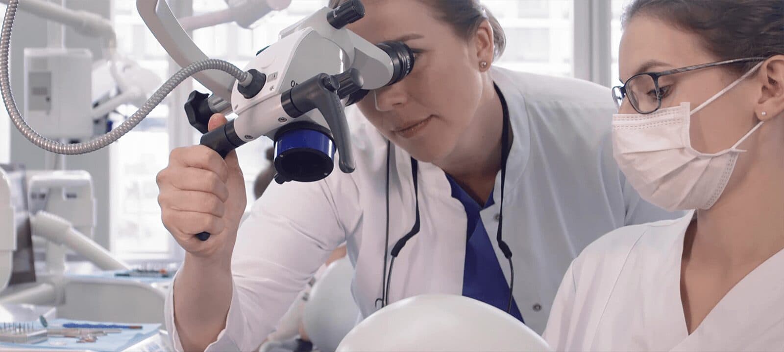 Two dental students at a dental microscope above a phantom head