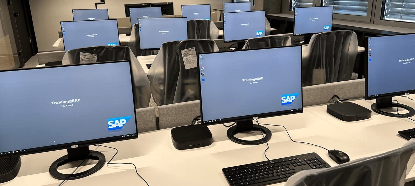 Student seats in a computer lab with monitors, keyboards and compact computers in rows